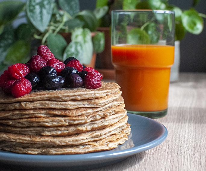 pille de pancakes avec des fruits rouges et un jus de fruit